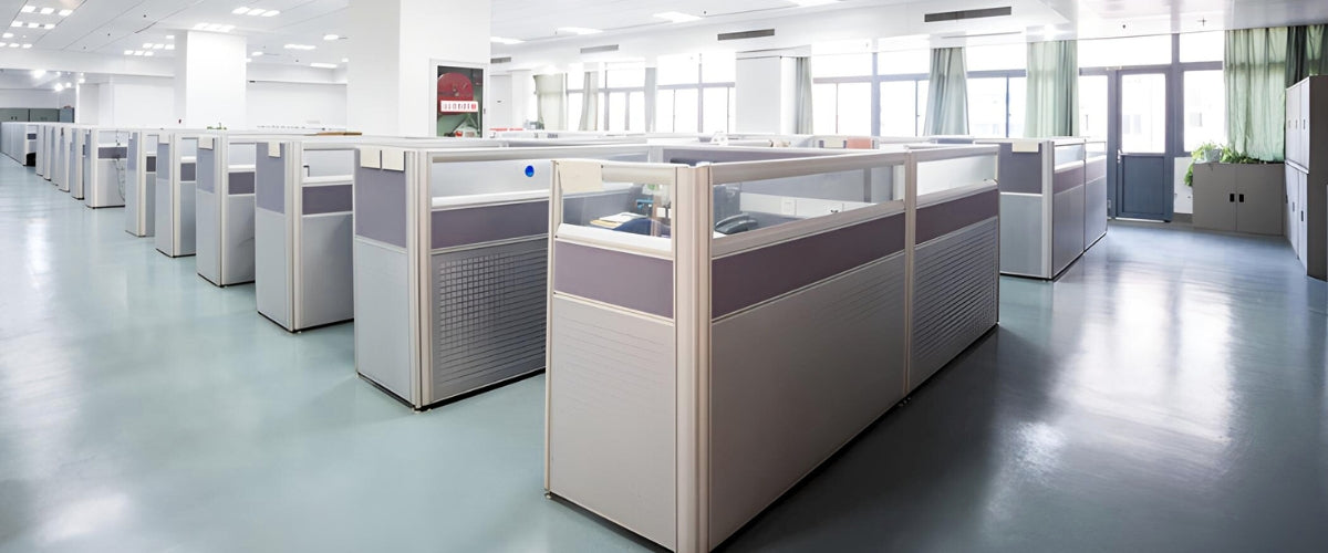 A spacious, well-lit office with rows of individual  cubicles separated by frosted glass office cubicle partition panels. The office cubicles are equipped with desks, chairs, and computers.