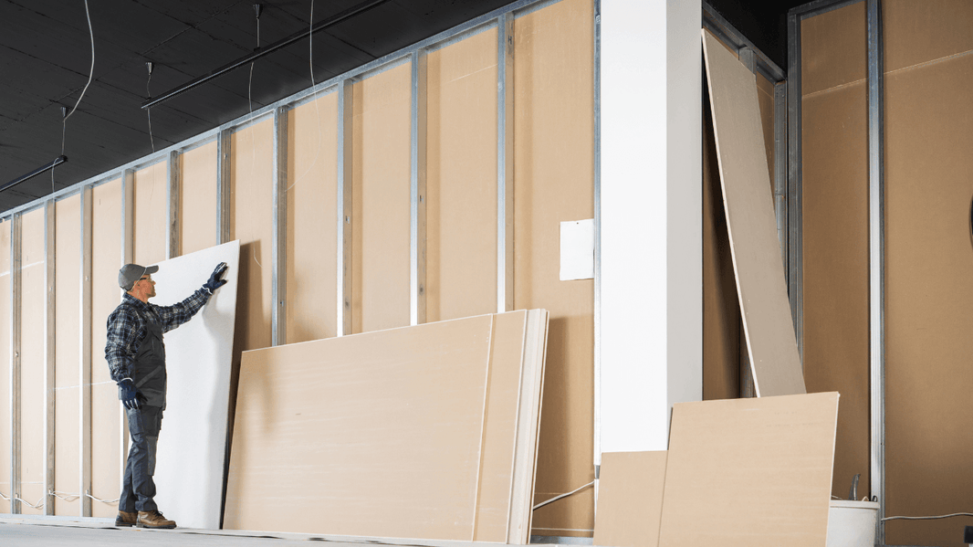 A worker installs a movable partition wall using large beige panels, preparing the framework for flexible space division in a modern building.