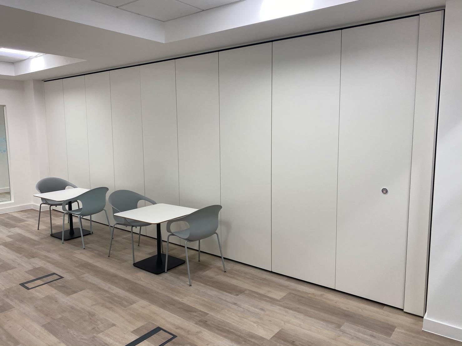 A foldable and movable partition wall in a well lit soundproof room with gray chairs and white tables