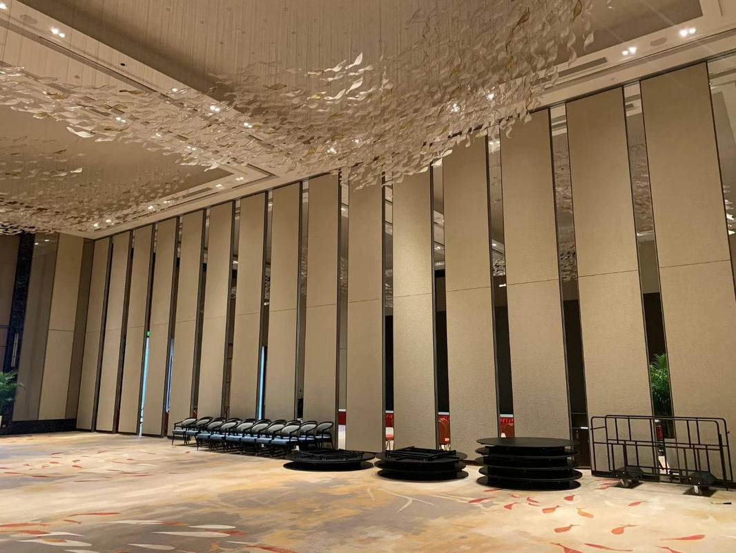 Large conference hall featuring a foldable partition wall with a tall, elegant design. The space includes stacked chairs and round platforms, with decorative ceiling elements enhancing the atmosphere.