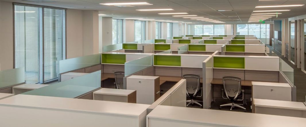 The image depicts a modern office space with rows of cubicles, featuring green accent panels and glass dividers.